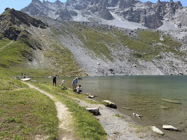 This photo captures a tranquil scene at Courchevel, where several people are gathered by the clear waters of a mountain lake